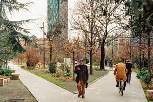 Tree-lined path with modern tower in background and people walking and cycling. Tirana, Albania,