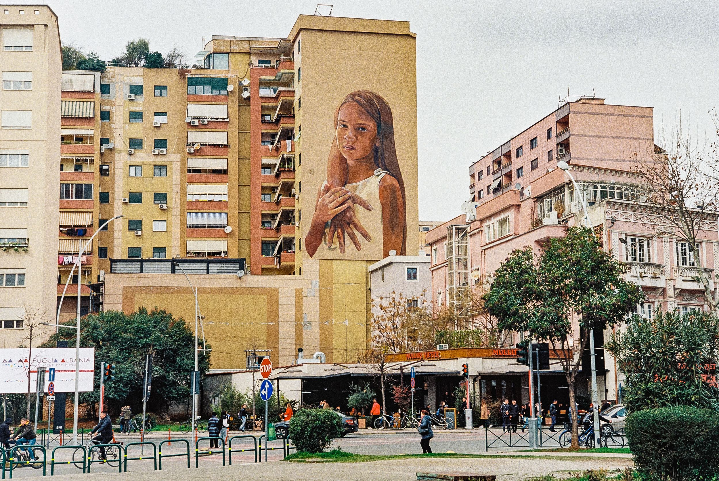 Large mural of a woman decorates apartment building facade in urban setting. Tirana, Albania,