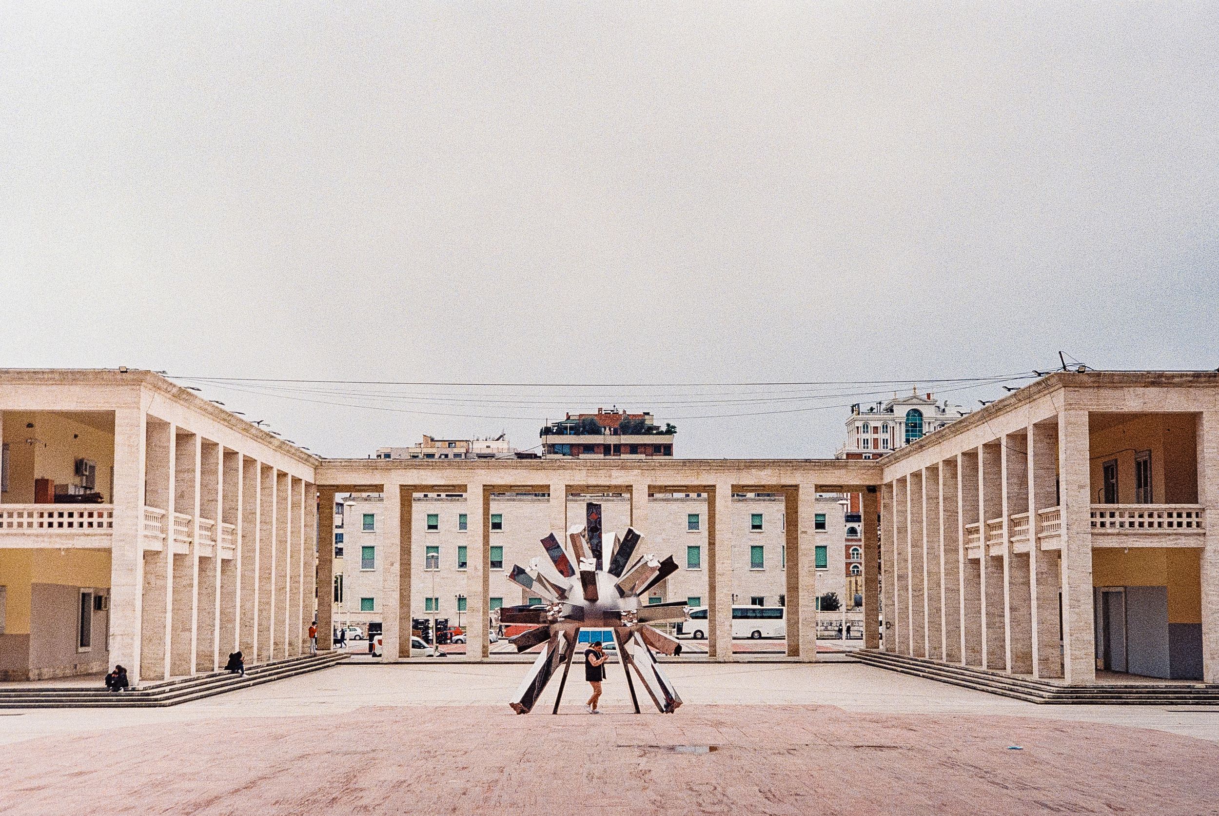 A vibrant street scene in Tirana, Albania, featuring colorful buildings, Skanderbeg Square, and the Et'hem Bey Mosque.