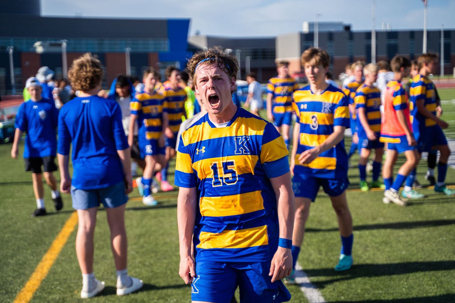 Soccer player celebrates enthusiastically in blue and yellow striped uniform.