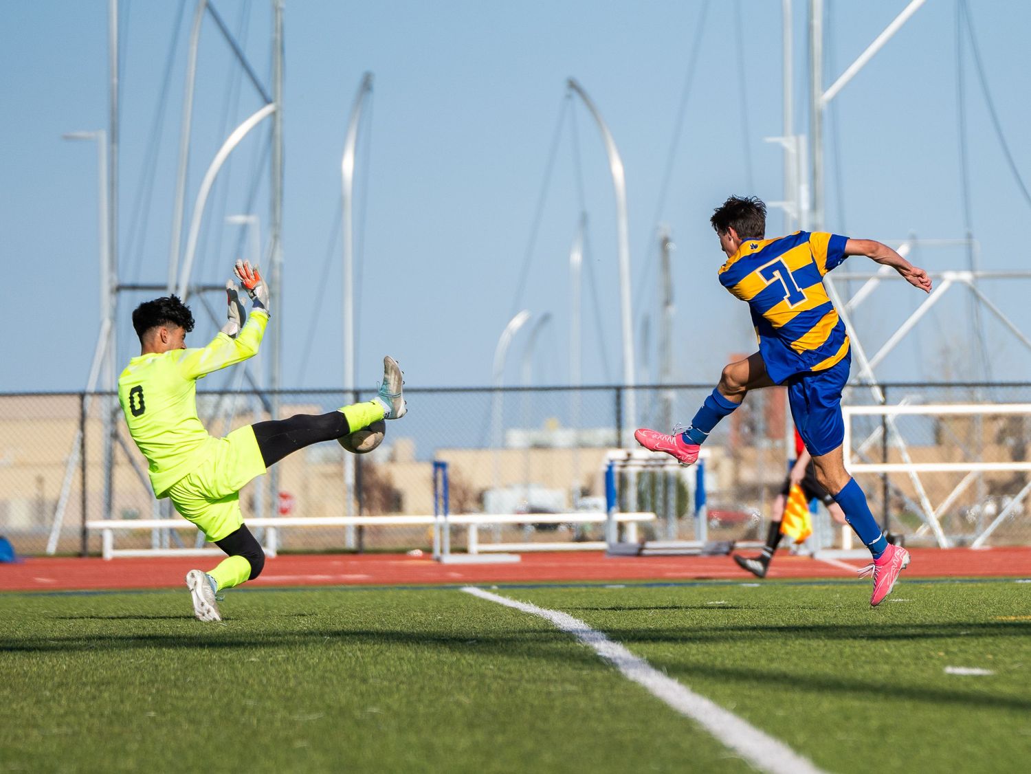 Soccer action shot shows goalkeeper diving to block shot from attacking player.