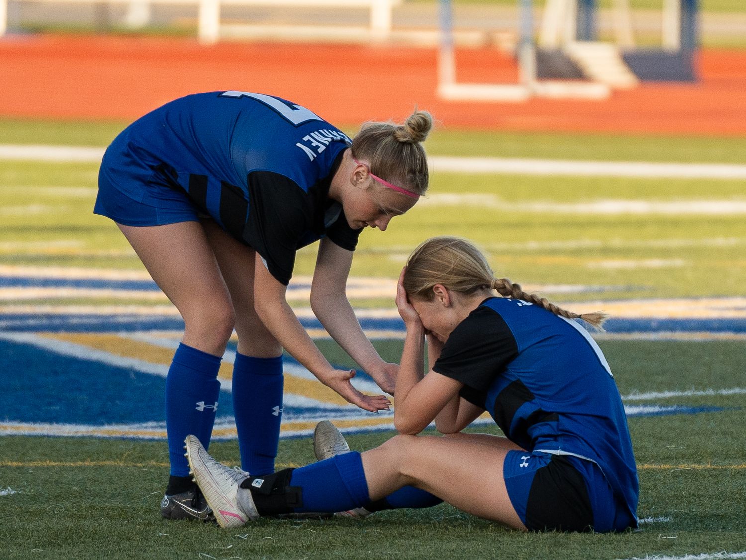 Soccer players attend to injured teammate on artificial turf field.