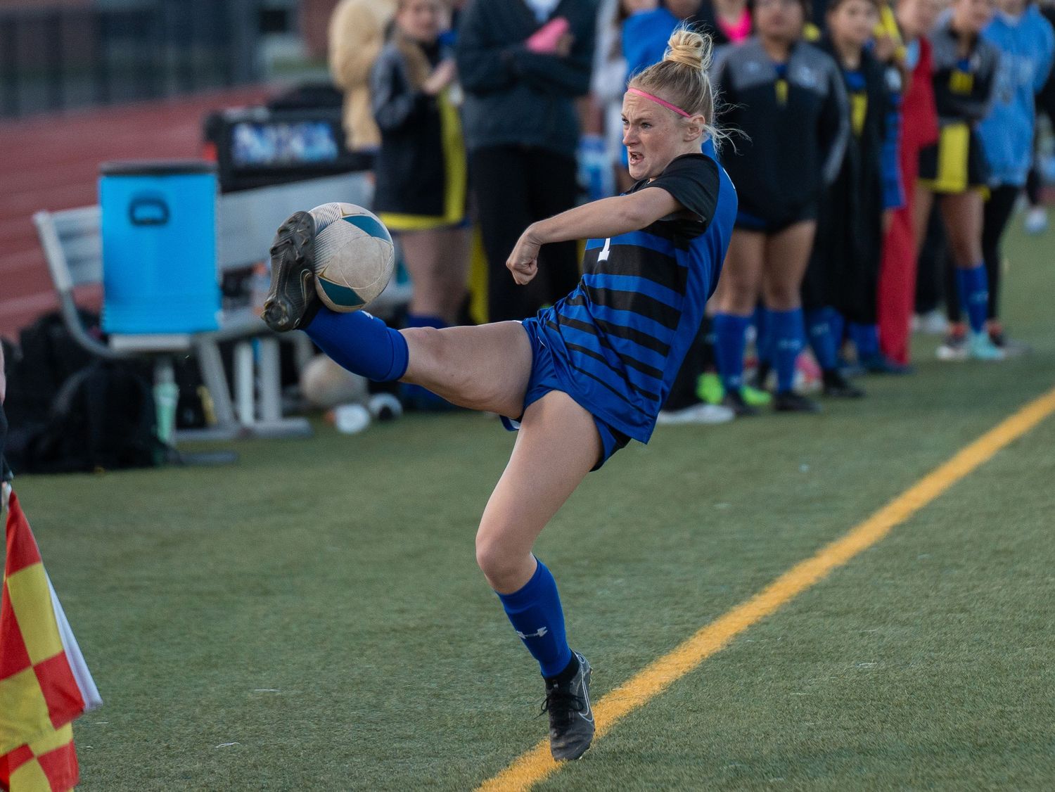 Soccer player in blue jersey performs a high kick during match on artificial turf.