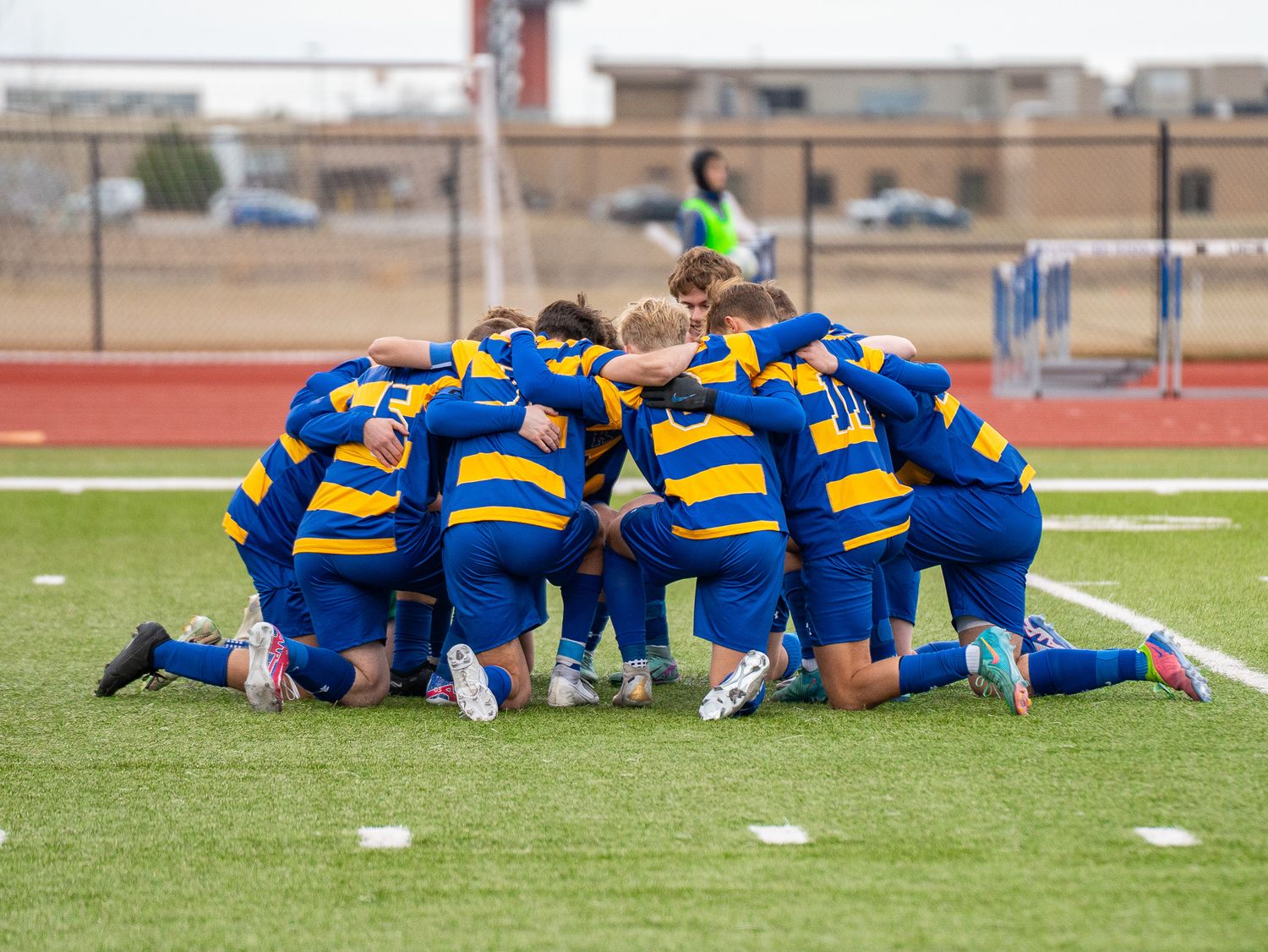 Soccer team in blue and yellow striped jerseys huddles together in prayer formation on field.