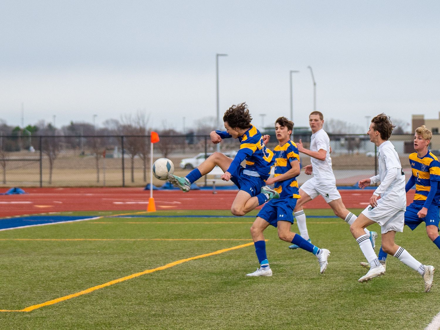 Soccer players leap for shot during competitive match on artificial turf field.
