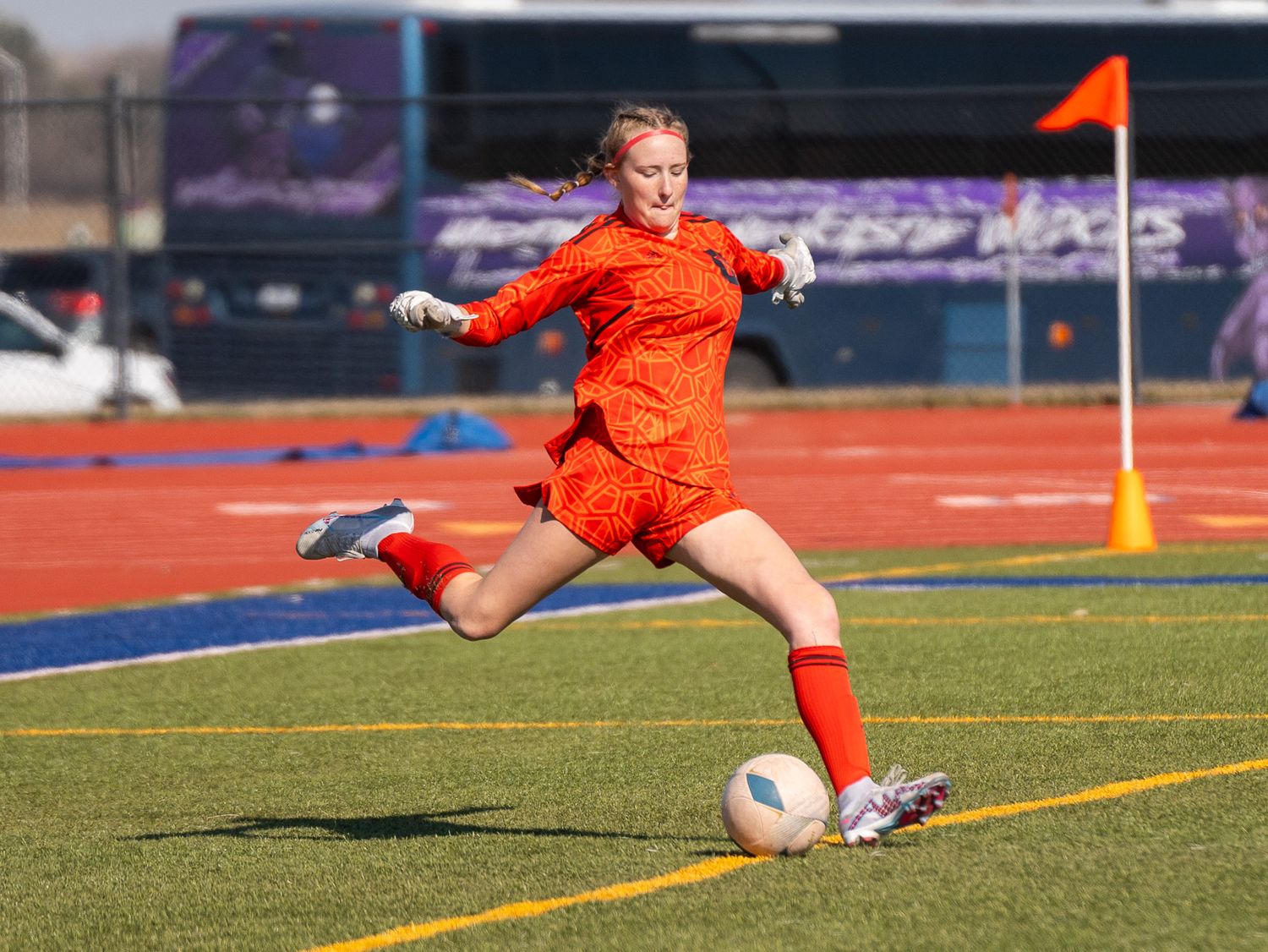 Soccer player in bright orange uniform takes powerful shot on field.