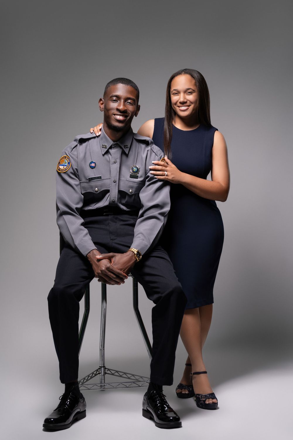 Studio portrait of police officer in uniform seated with companion in navy dress.