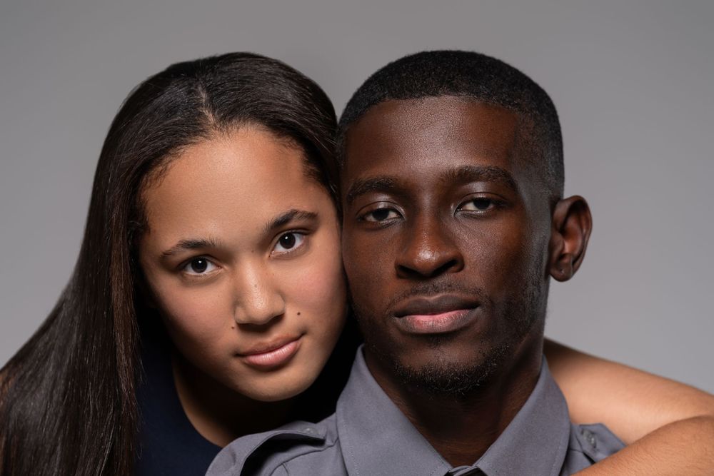 Intimate studio portrait of a couple in formal attire against a dark grey background.