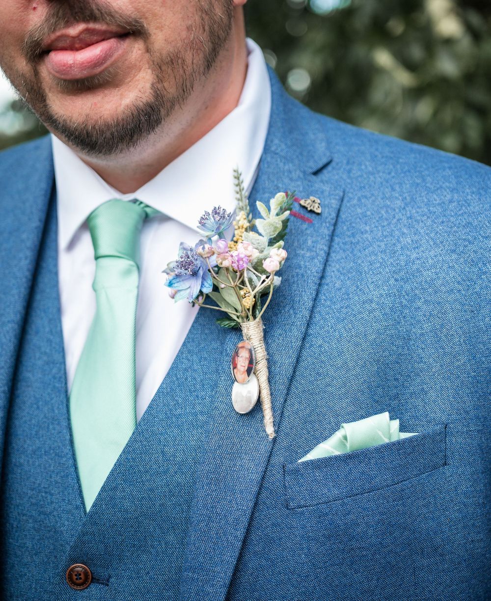 Close-up of blue suit jacket with mint green tie and delicate floral boutonniere.