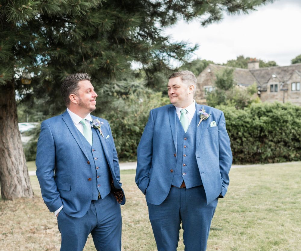 Two people in matching blue three-piece suits share a candid moment outdoors.