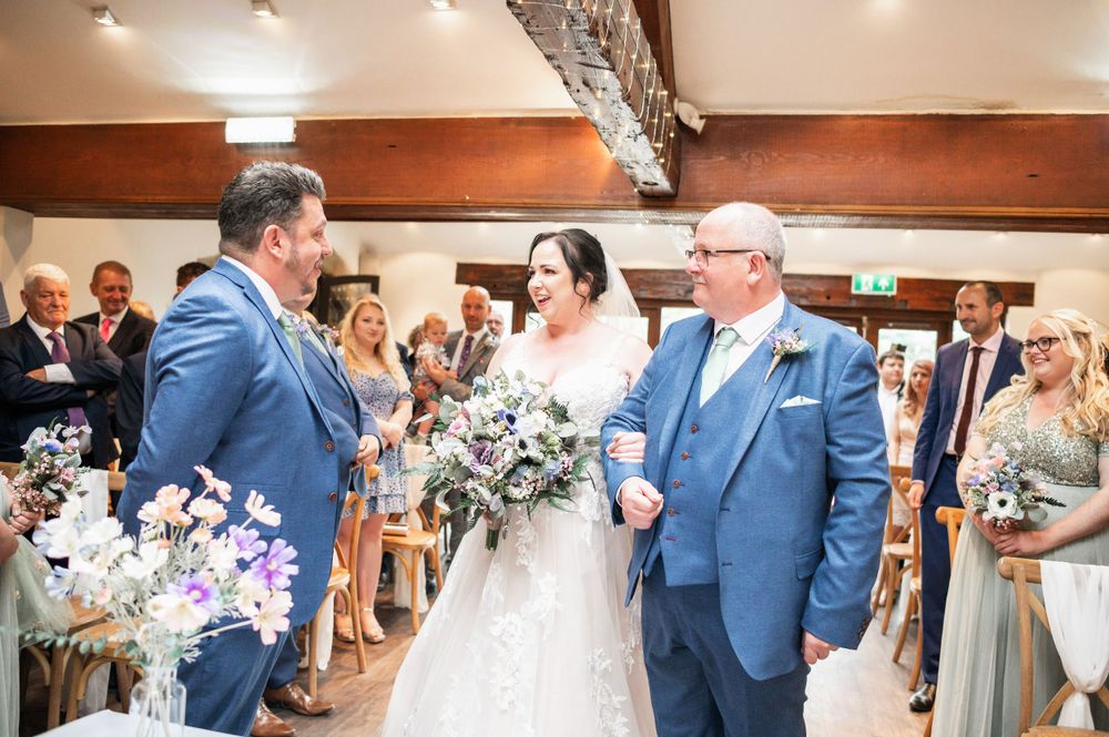 Wedding ceremony in progress inside rustic venue with wooden beams and gathered guests.