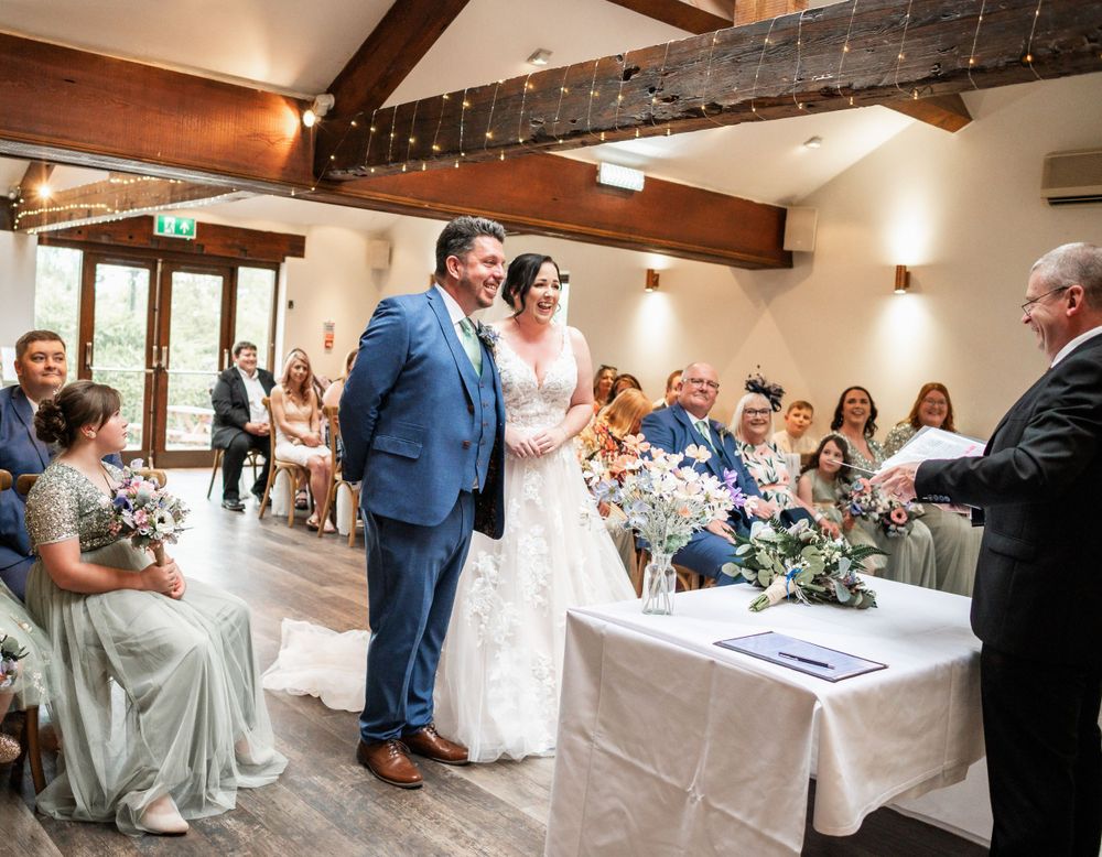 Wedding ceremony taking place in a rustic venue with exposed wooden beams and gathered guests.