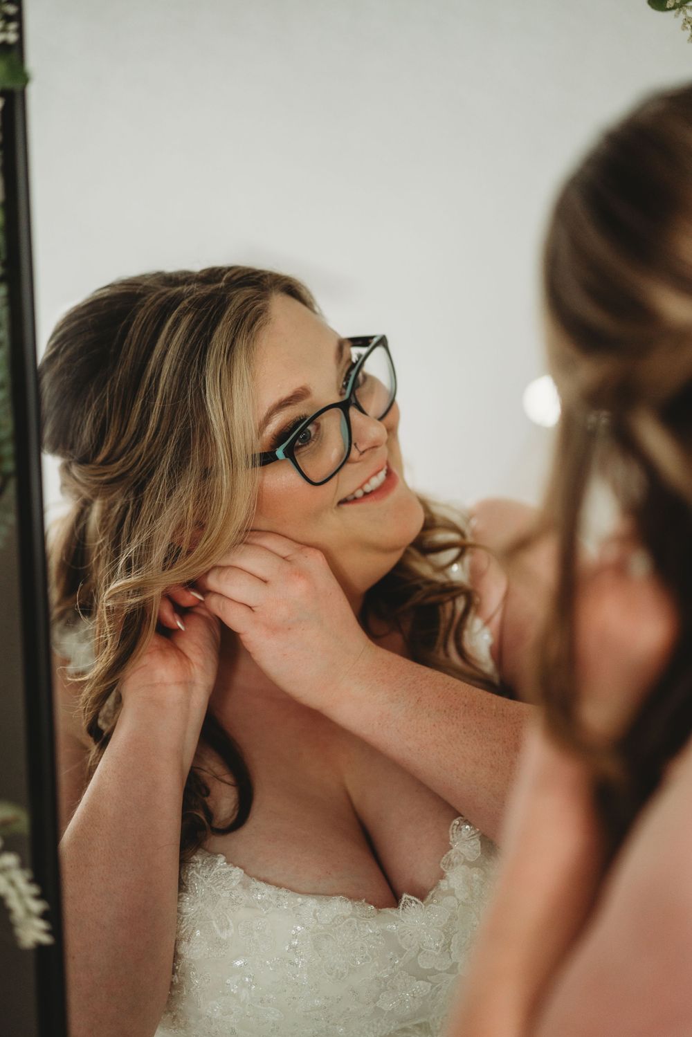 Bride with glasses checking her hair and makeup in mirror.