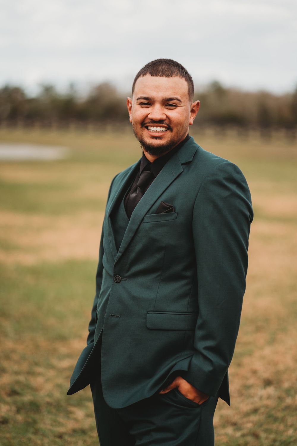 Formal portrait of groom in dark green suit jacket outdoors.