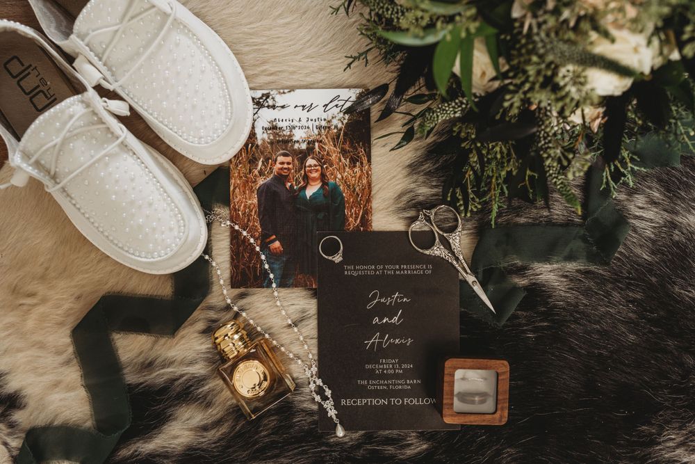 Wedding details flatlay with white shoes, invitation, rings and greenery.