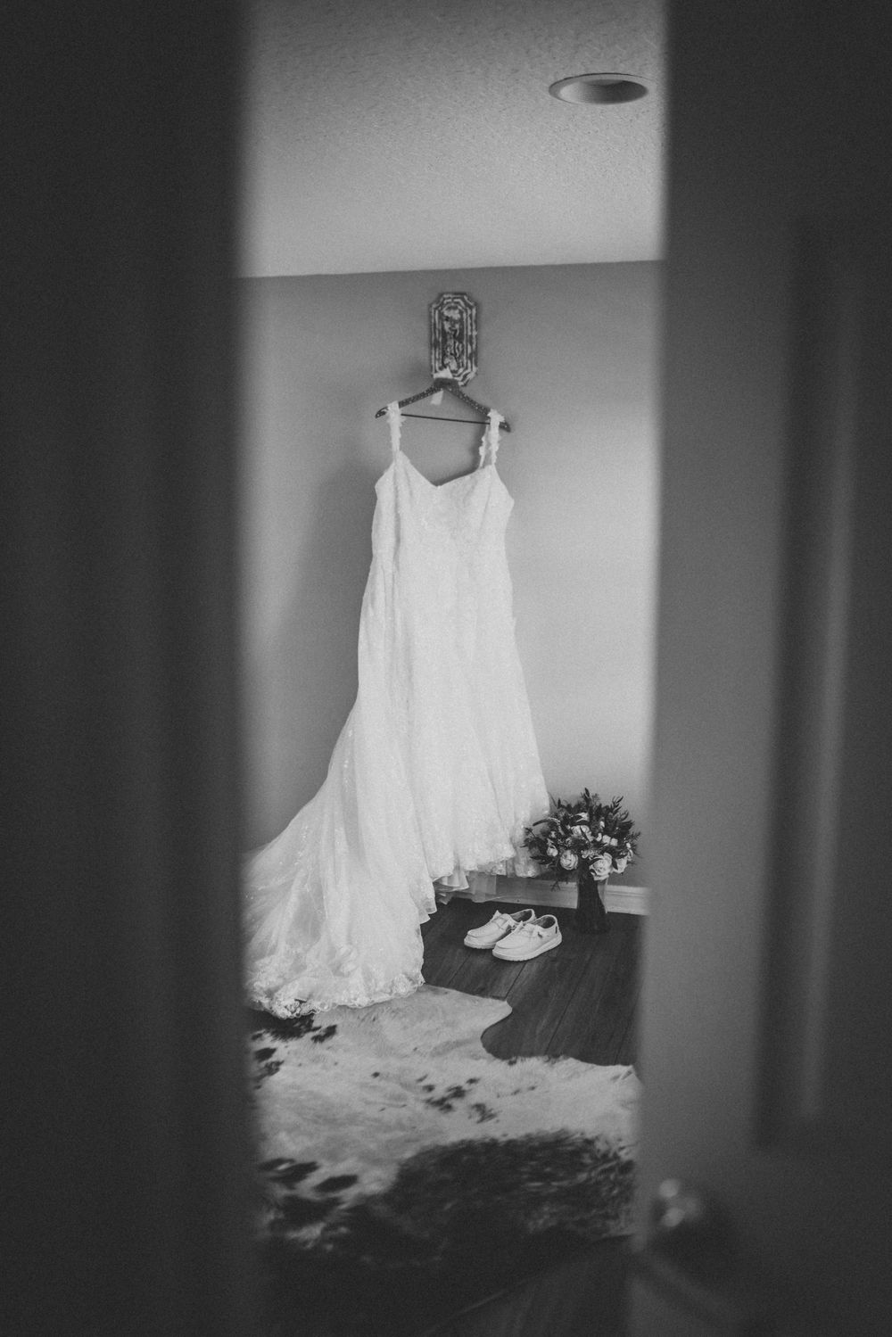 Wedding dress hanging in doorway with shoes and bouquet in black and white.