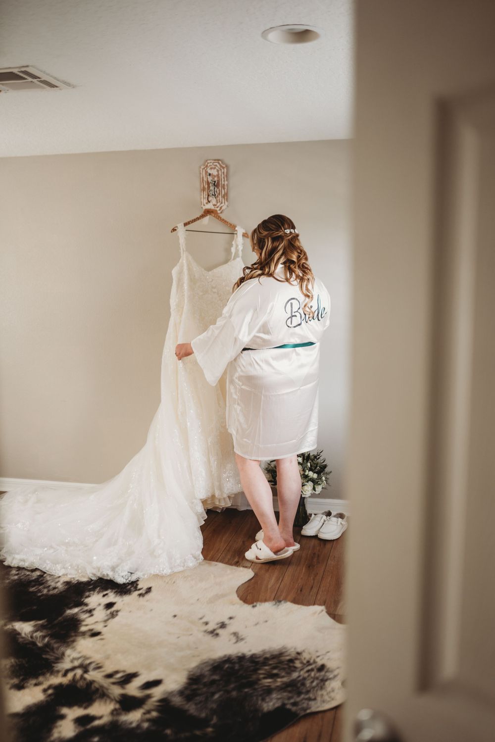 Wedding dress hanging in room while bride in robe prepares for ceremony.