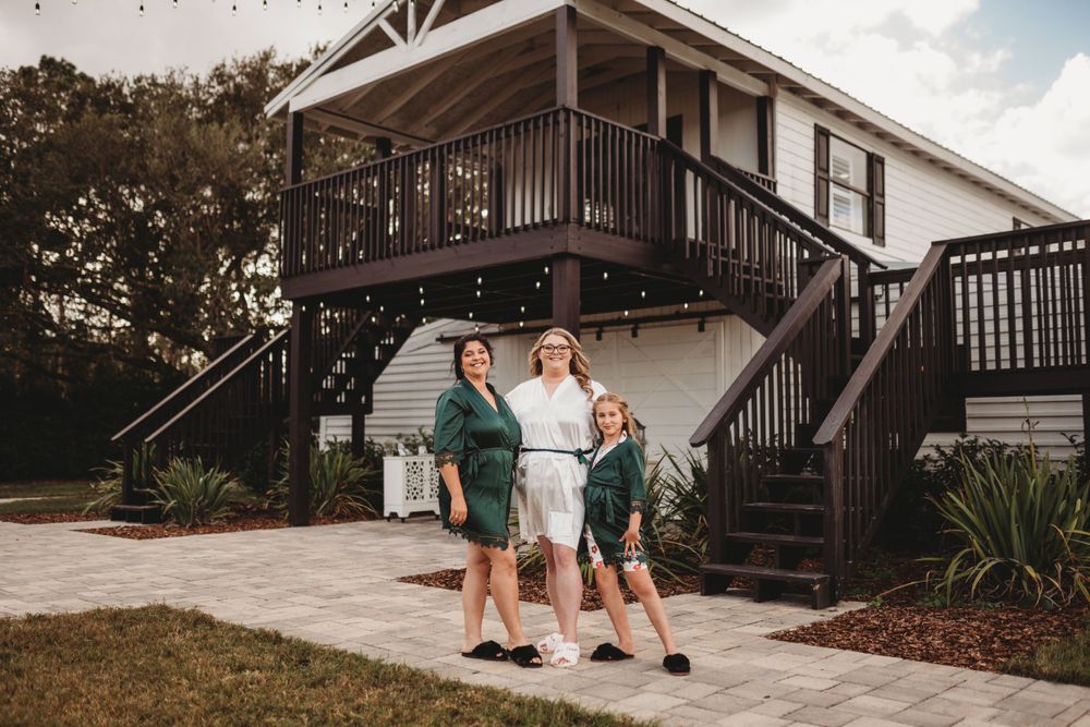 Three people standing outside elevated house with wooden stairs and deck.