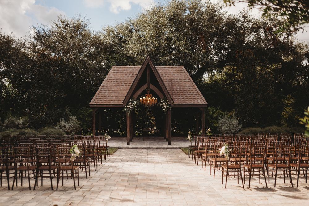 Rustic wooden gazebo with rows of brown chairs set up for an outdoor wedding ceremony.