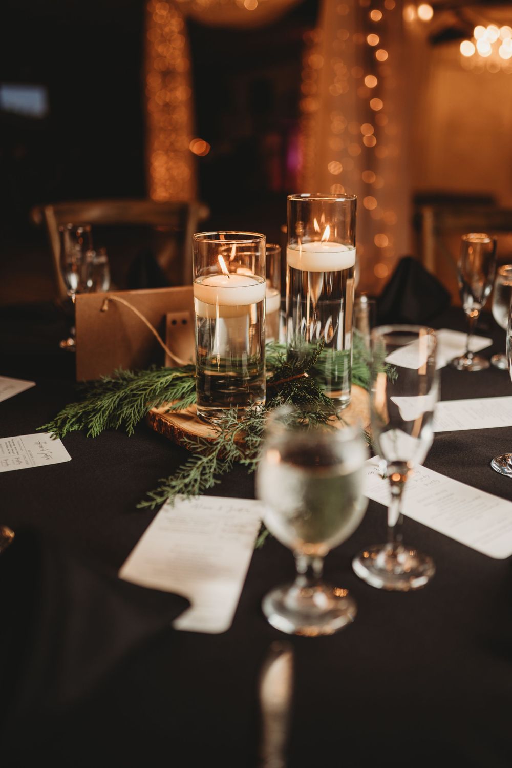 Elegant table setting with floating candles and evergreen sprigs at wedding reception.