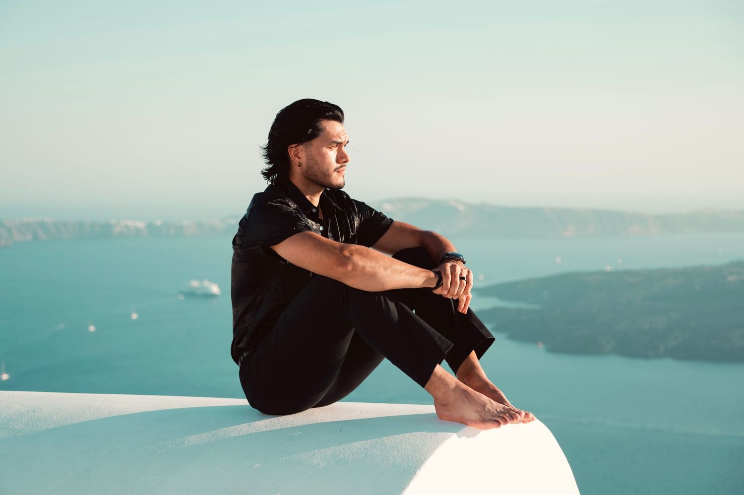 A traveler sits on a white ledge overlooking the Mediterranean coastline and blue waters.