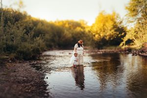 Golden hour family photos by river with trees in autumn colors.