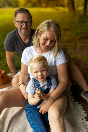 Happy family enjoying outdoor picnic on blanket in sunlit park setting.