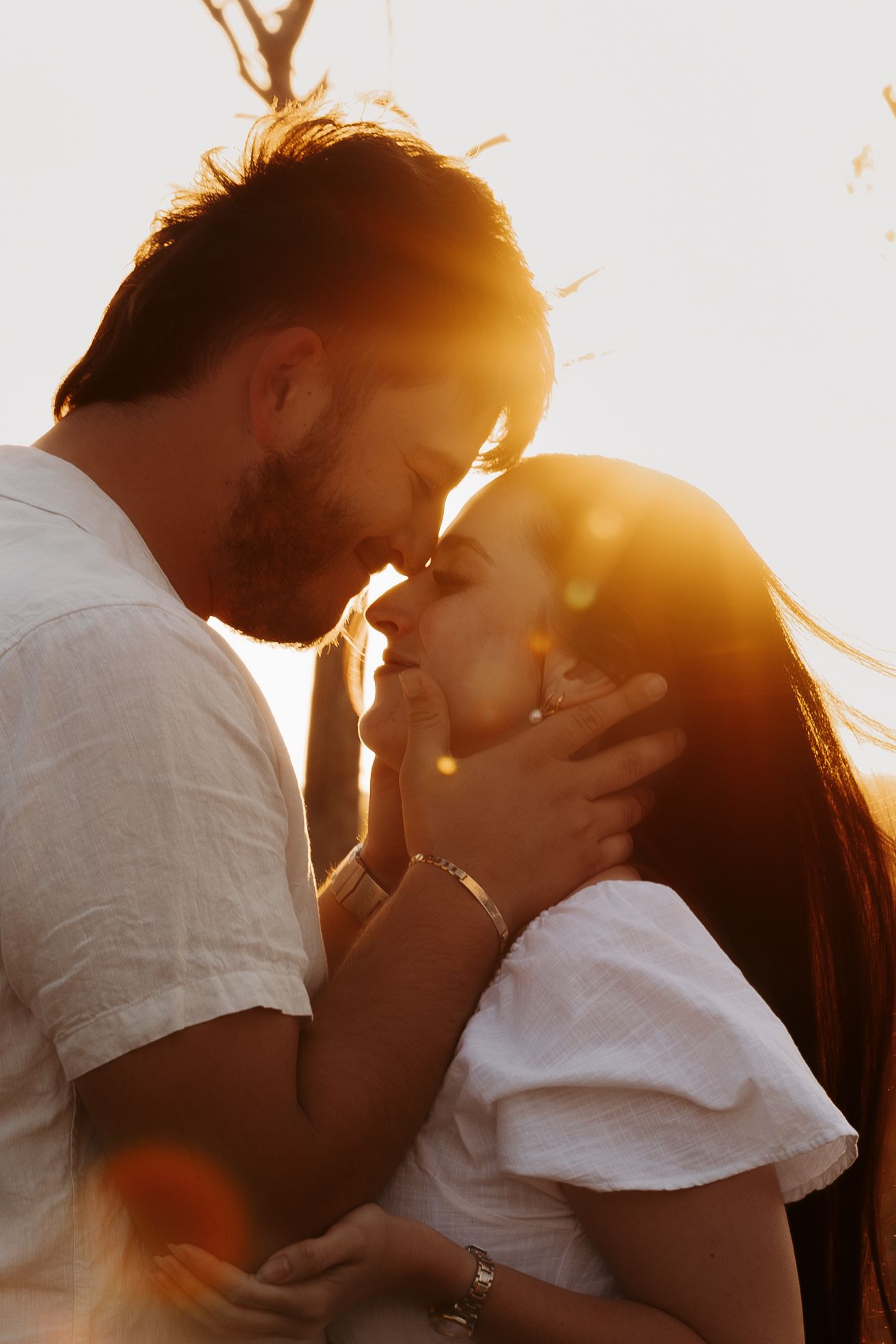 Romantic couple embraces in warm golden sunlight creating a dreamy silhouette against sunset background.