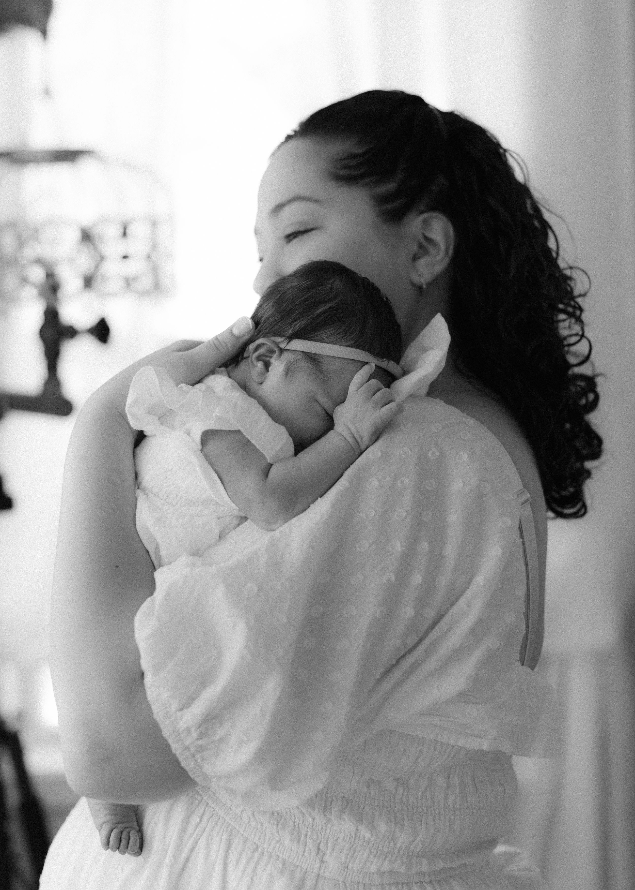 A tender black and white portrait of parent and baby sharing an intimate moment while dressed in white.