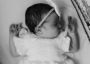 A sleeping baby in white clothing rests peacefully on white bedding in black and white photography.