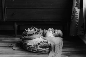 A person lies still on the hardwood floor beside an antique quilt in a black and white photograph.