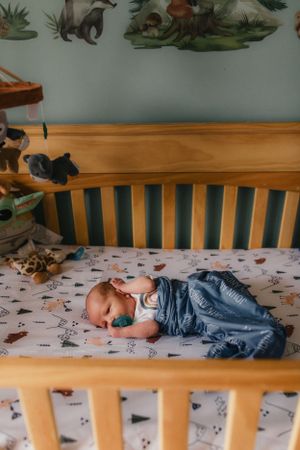 Baby sleeping peacefully in wooden crib with animal-themed decor and patterned bedding.
