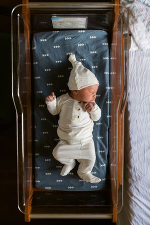 Overhead view of newborn baby in white outfit lying on dark patterned blanket during growth progress photo series.