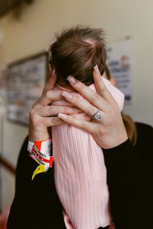 Person covering face with hands wearing pink sweater and ring against blurred background.