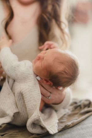 A newborn baby in a soft white sweater lies peacefully in a tender moment against a blurred background.