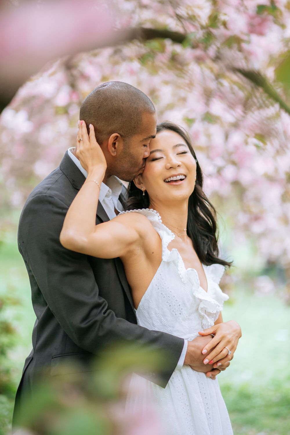 A romantic moment captured under blooming cherry blossoms with a couple embracing in wedding attire.