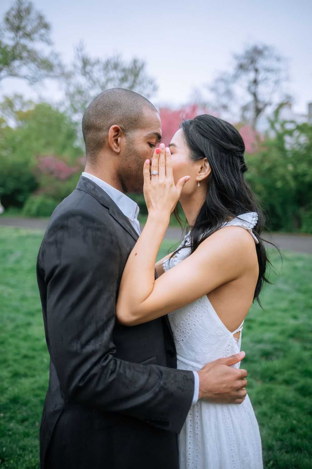 A romantic outdoor moment between a couple in formal attire sharing a whispered secret in a garden setting.