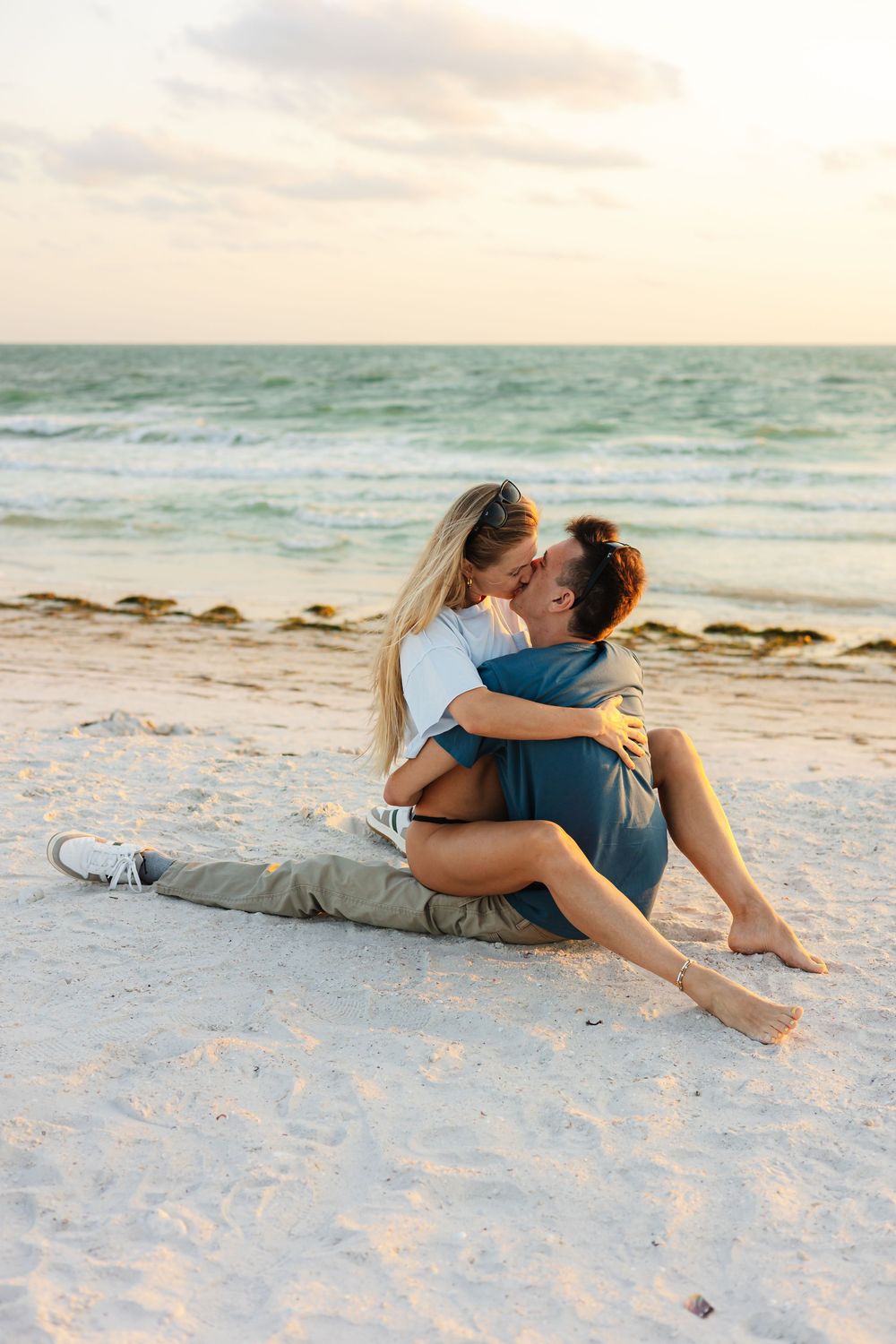 A romantic couple embraces on a serene beach at sunset with turquoise waves and sand creating a peaceful backdrop.