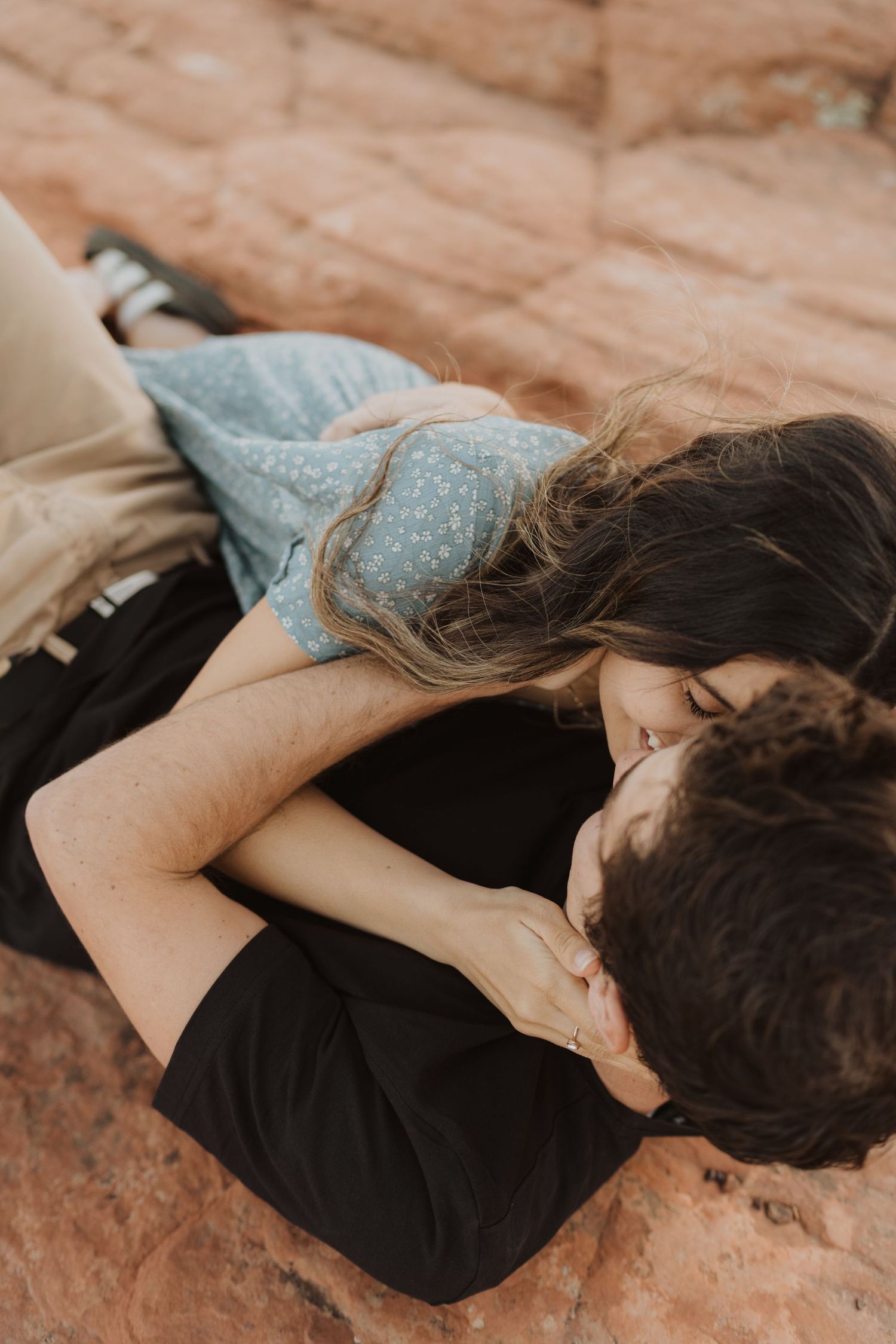 Couple lying together on red rock formations in casual attire.