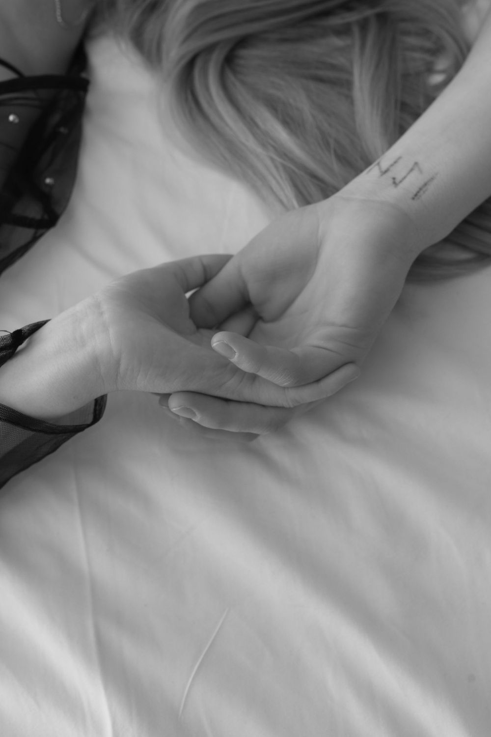 Black and white close up of hands clasped tenderly on white sheets.