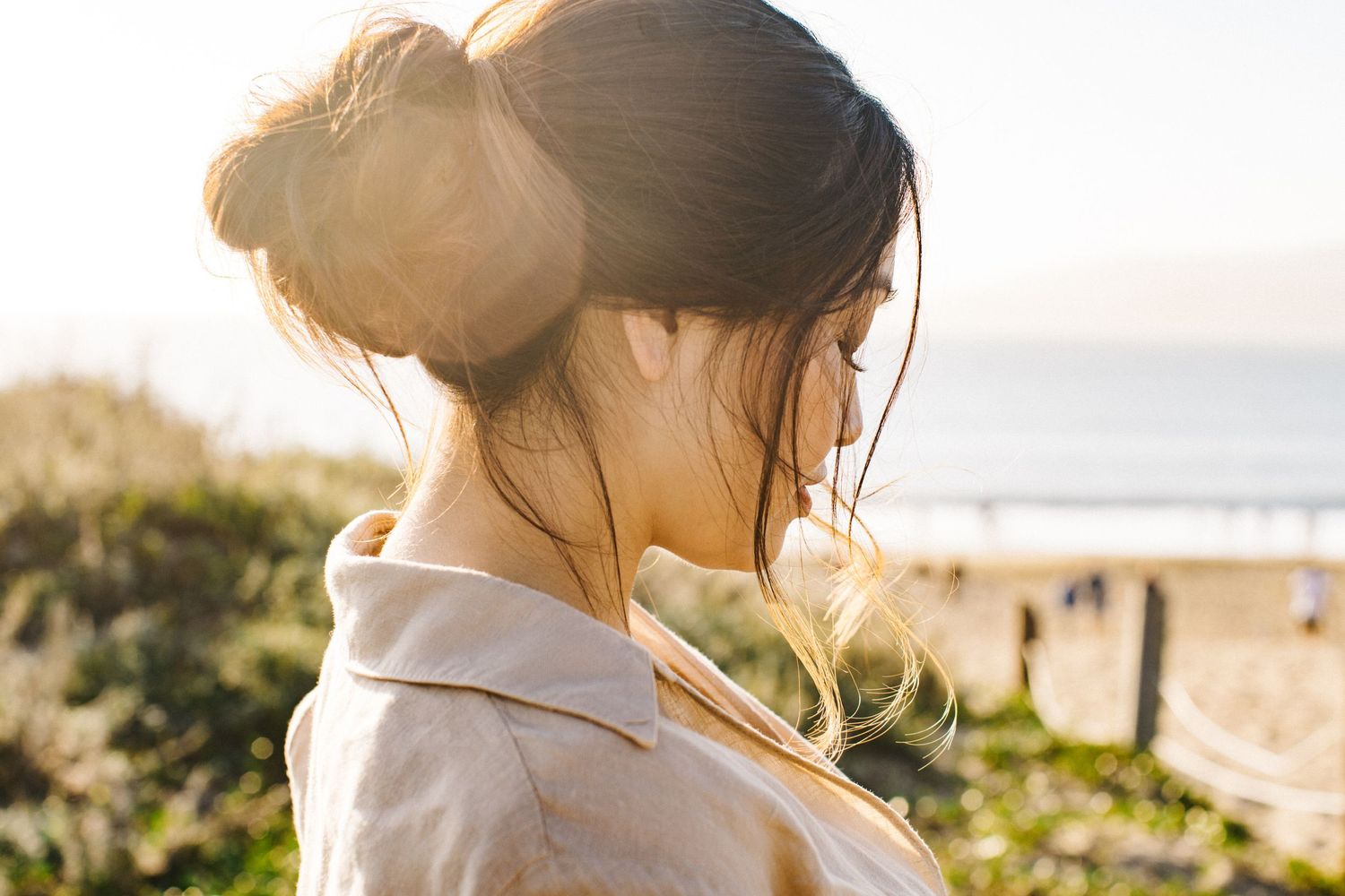 Backlit portrait of woman with upswept hair against beach landscape.