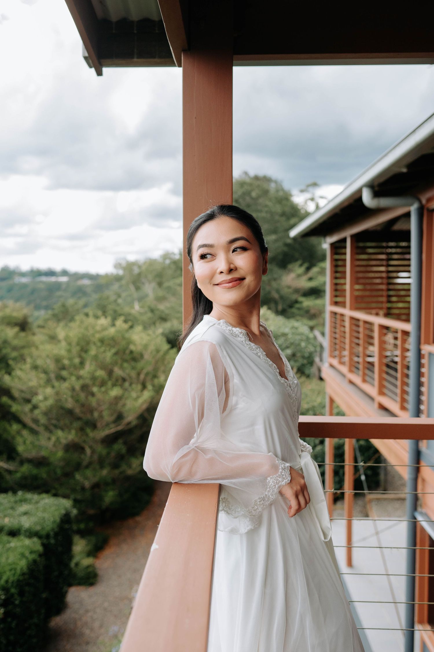 A bride in a flowing white dress poses on a balcony overlooking a lush landscape.