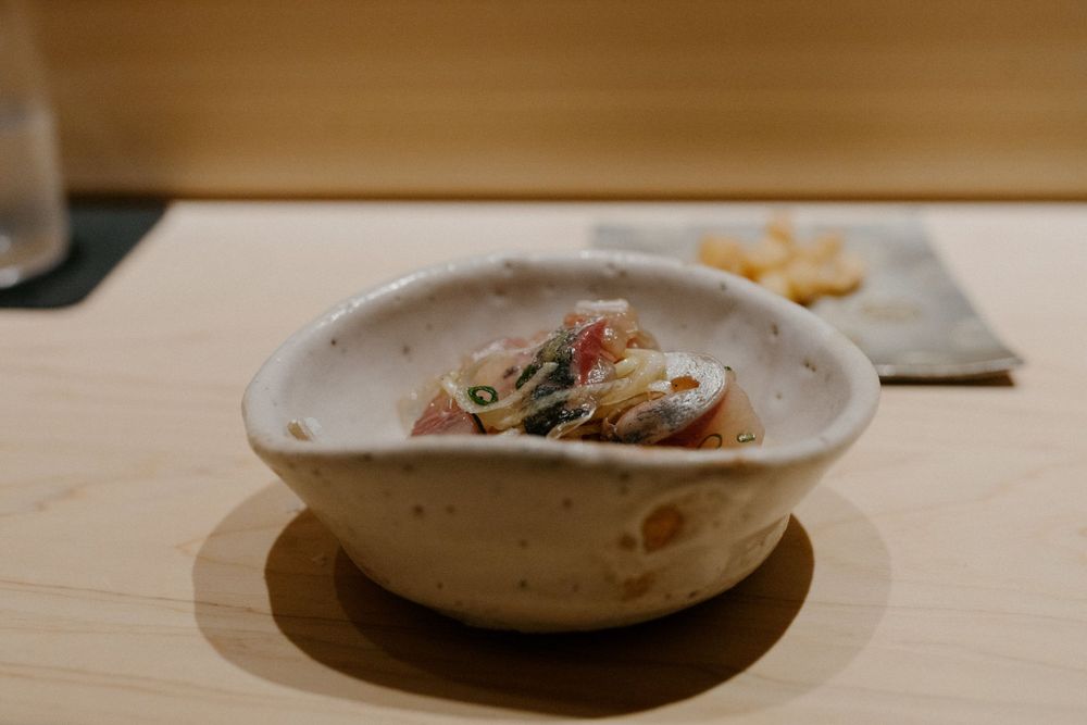 A ceramic bowl containing fresh seafood dish with garnishes on a wooden counter.