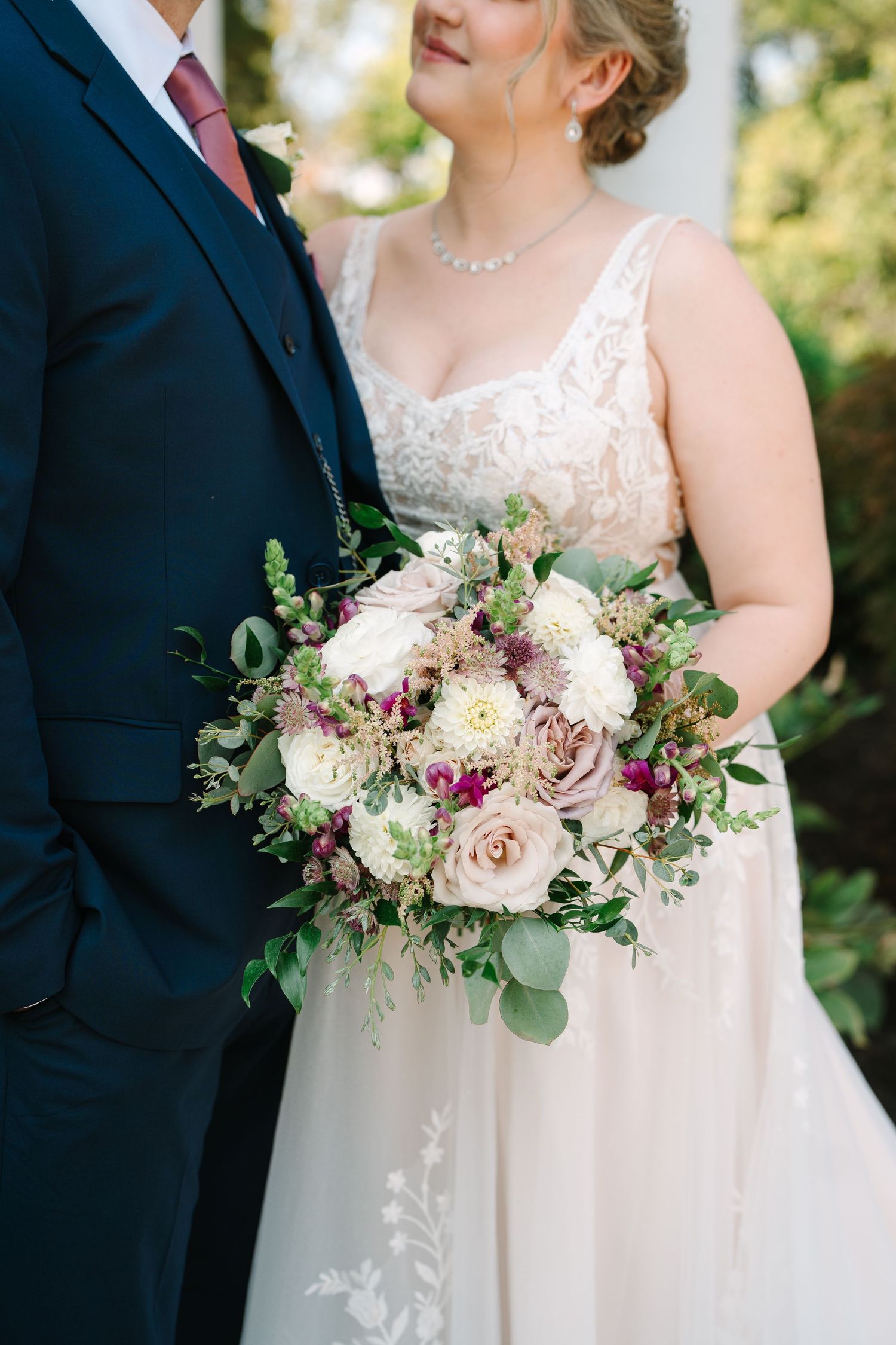 Close-up of romantic bridal bouquet with pink roses and greenery against formal attire.
