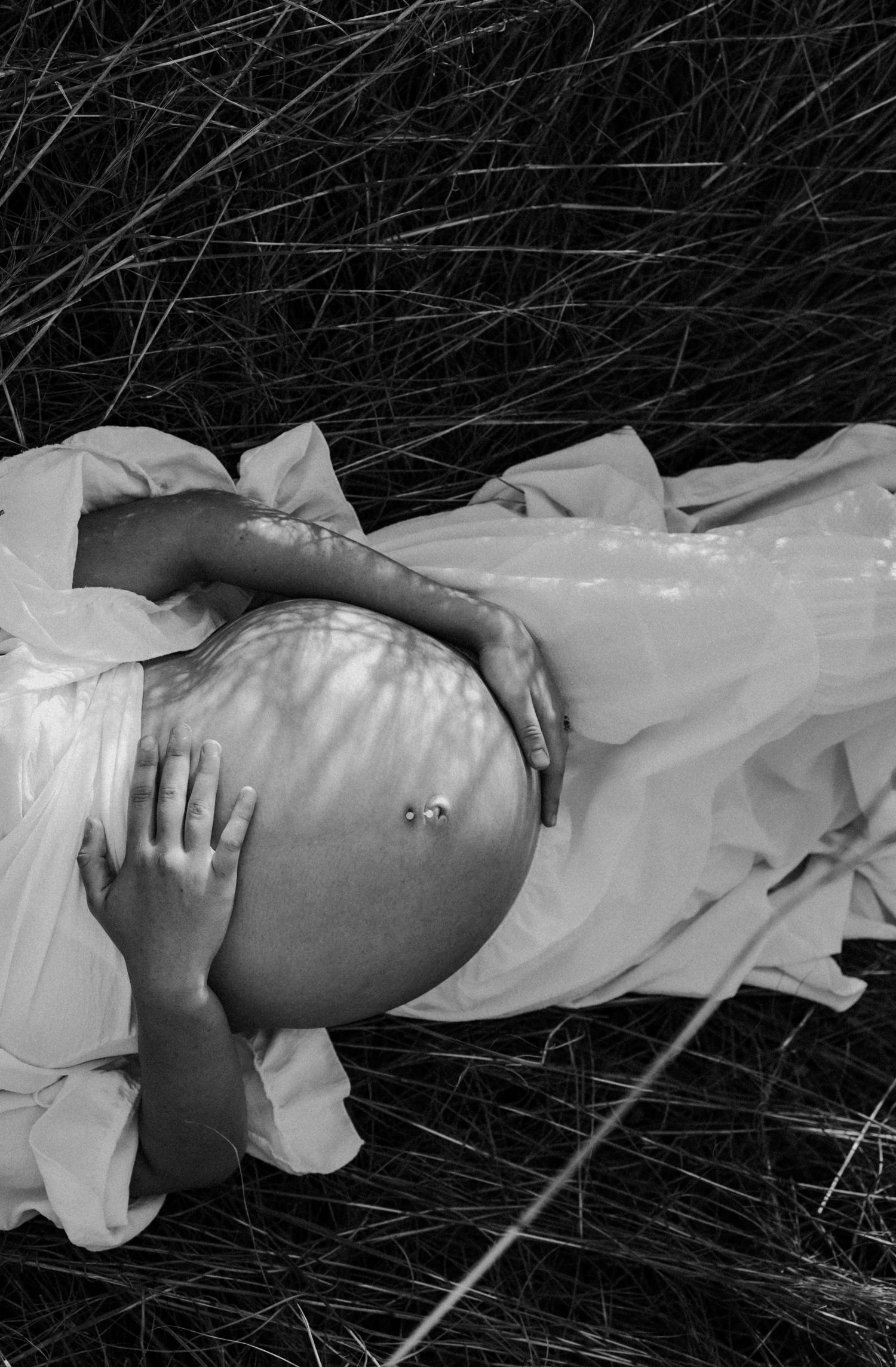 Artistic black and white close-up of pregnant belly with floral shadow patterns.