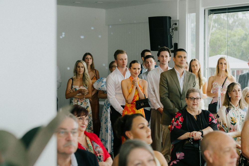 Wedding guests watching ceremony in bright modern indoor venue.