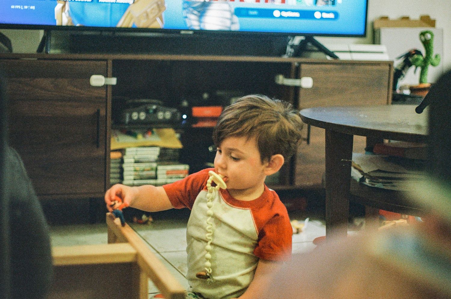 Child in orange shirt playing with toys near entertainment center.
