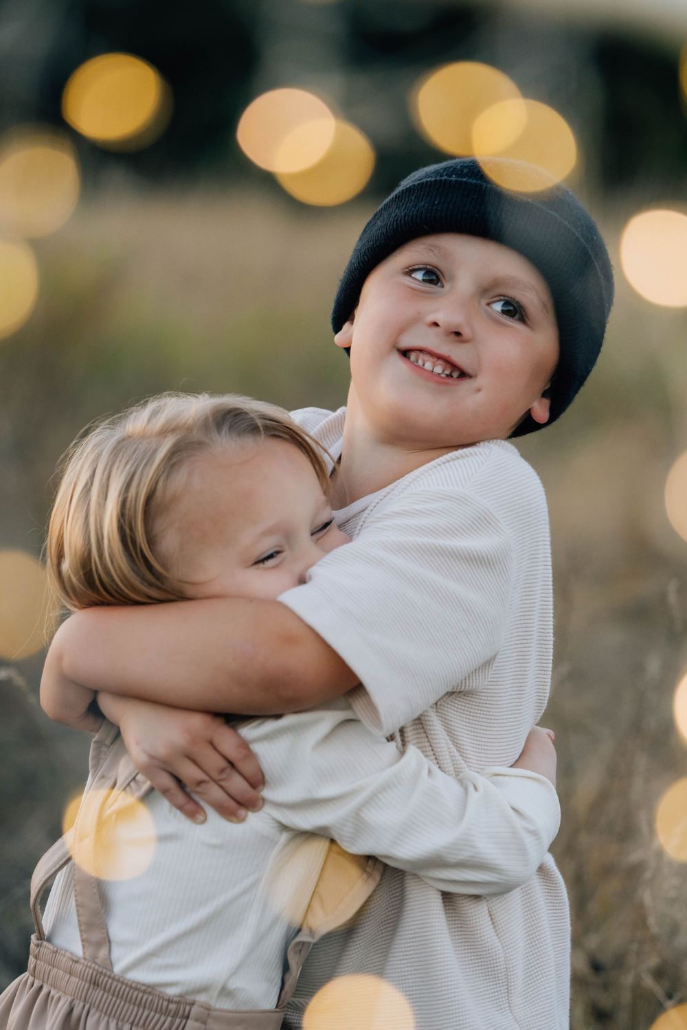 Two young siblings sharing a warm hug outdoors with bokeh lights in the background.