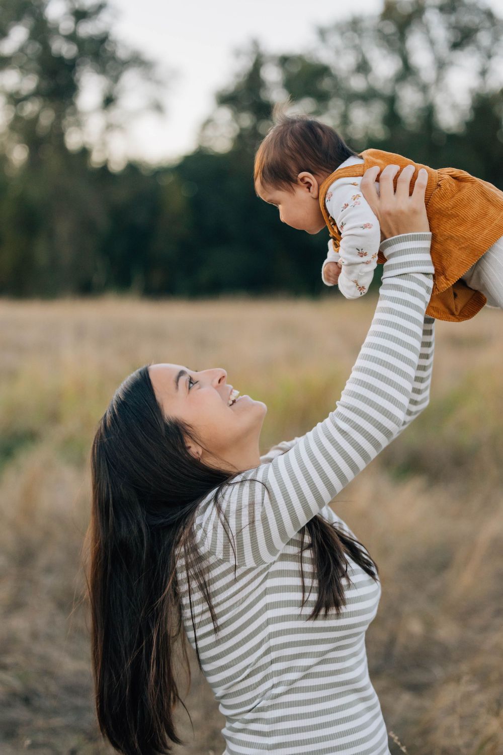 Joyful mother lifting her baby in the air in a sunlit autumn field.