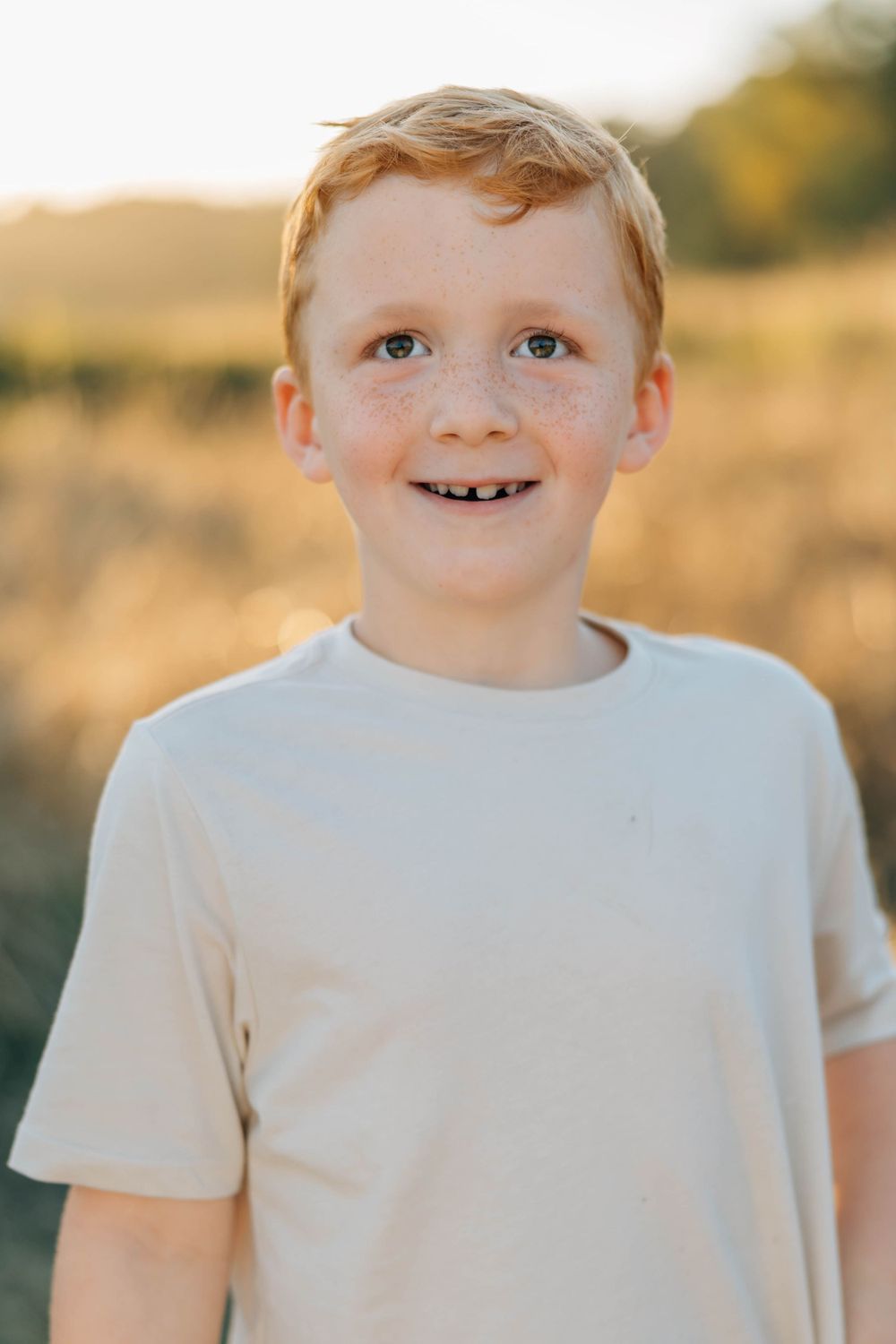 Adorable red-haired freckled boy smiling with missing tooth in sunny outdoor field.
